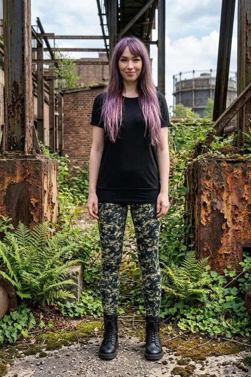 Frau mit lila Haaren trägt nachhaltige gemusterte Leggings, schwarzes Shirt und Boots in urbaner Umgebung