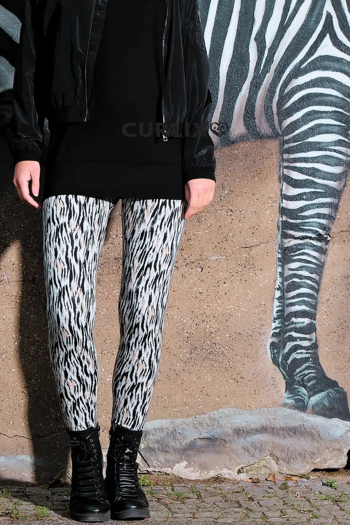 Frau trägt Leggings mit Zebramuster, schwarze Boots, vor Wand mit Zebramalerei