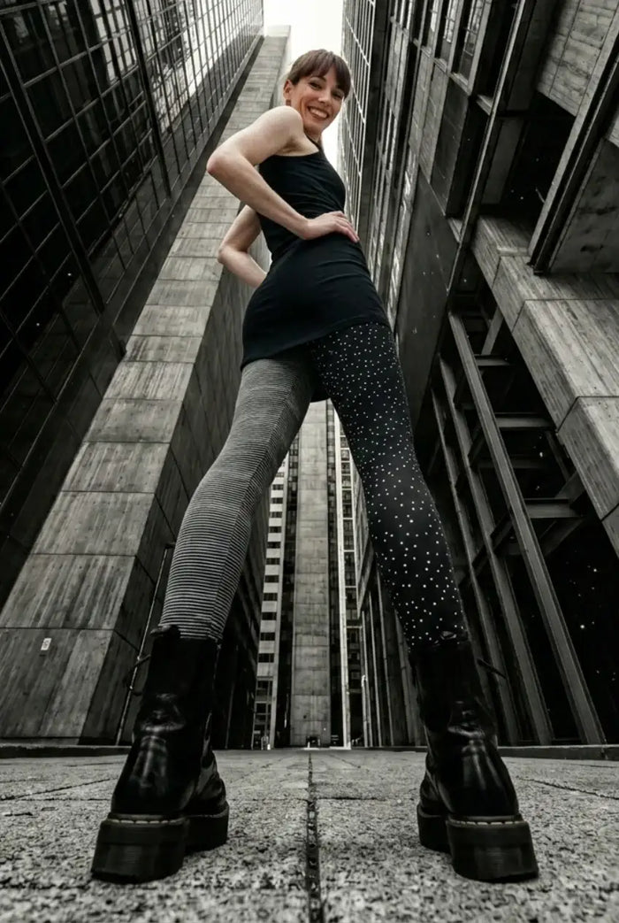 Frau in Harlekin-Baumwoll-Leggings mit Streifen und Punkten, urbanes Architektur-Setting, Modefoto