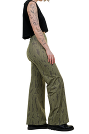 Frau mit olivgrüner Marlenehose mit floralem Muster und schwarzem Crop-Top, Seitenansicht
