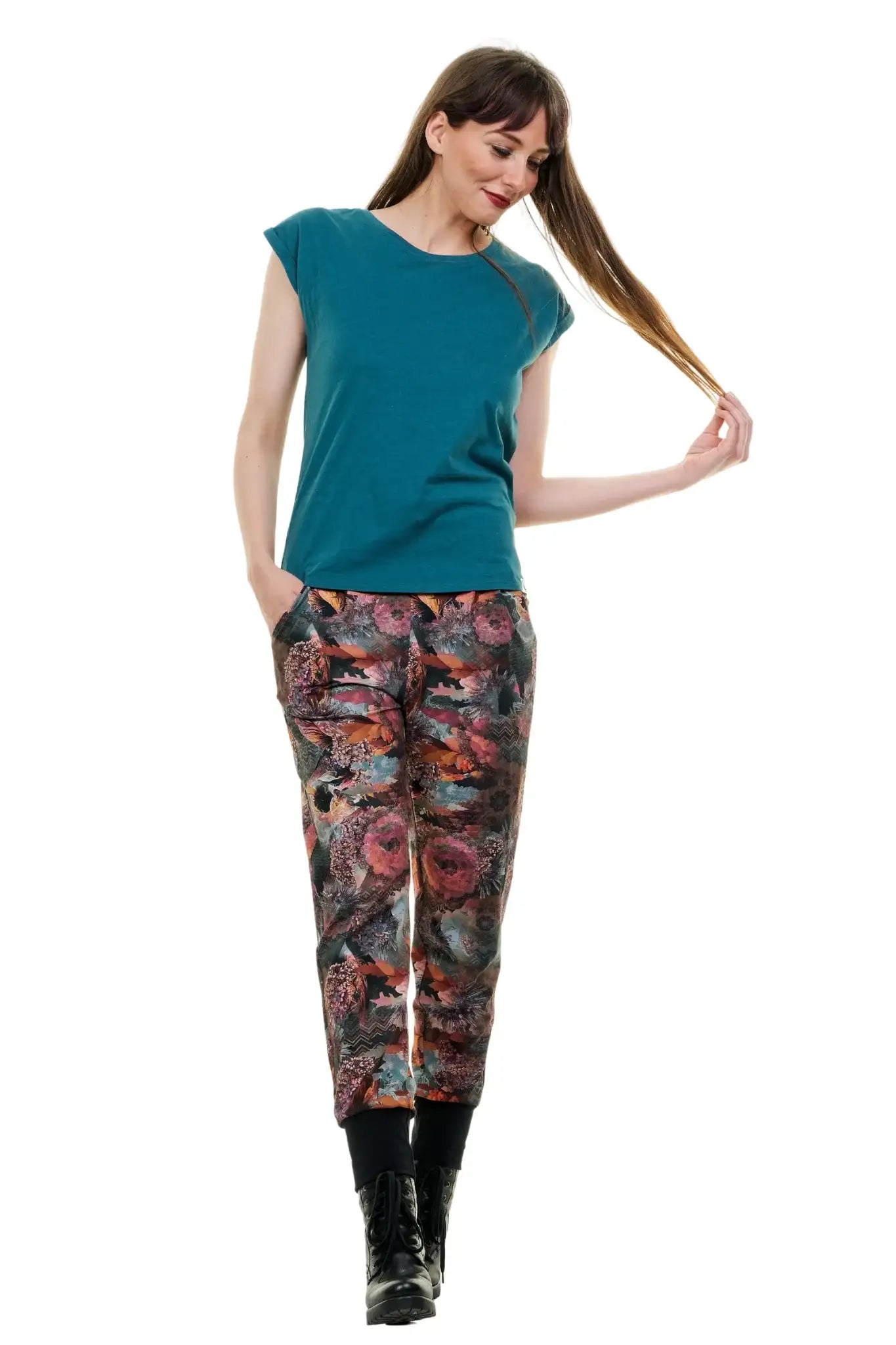 Damen trägt florale Jogginghose in Baggy-Passform mit rosa-rot Muster, schwarze Stiefel, weißer Hintergrund