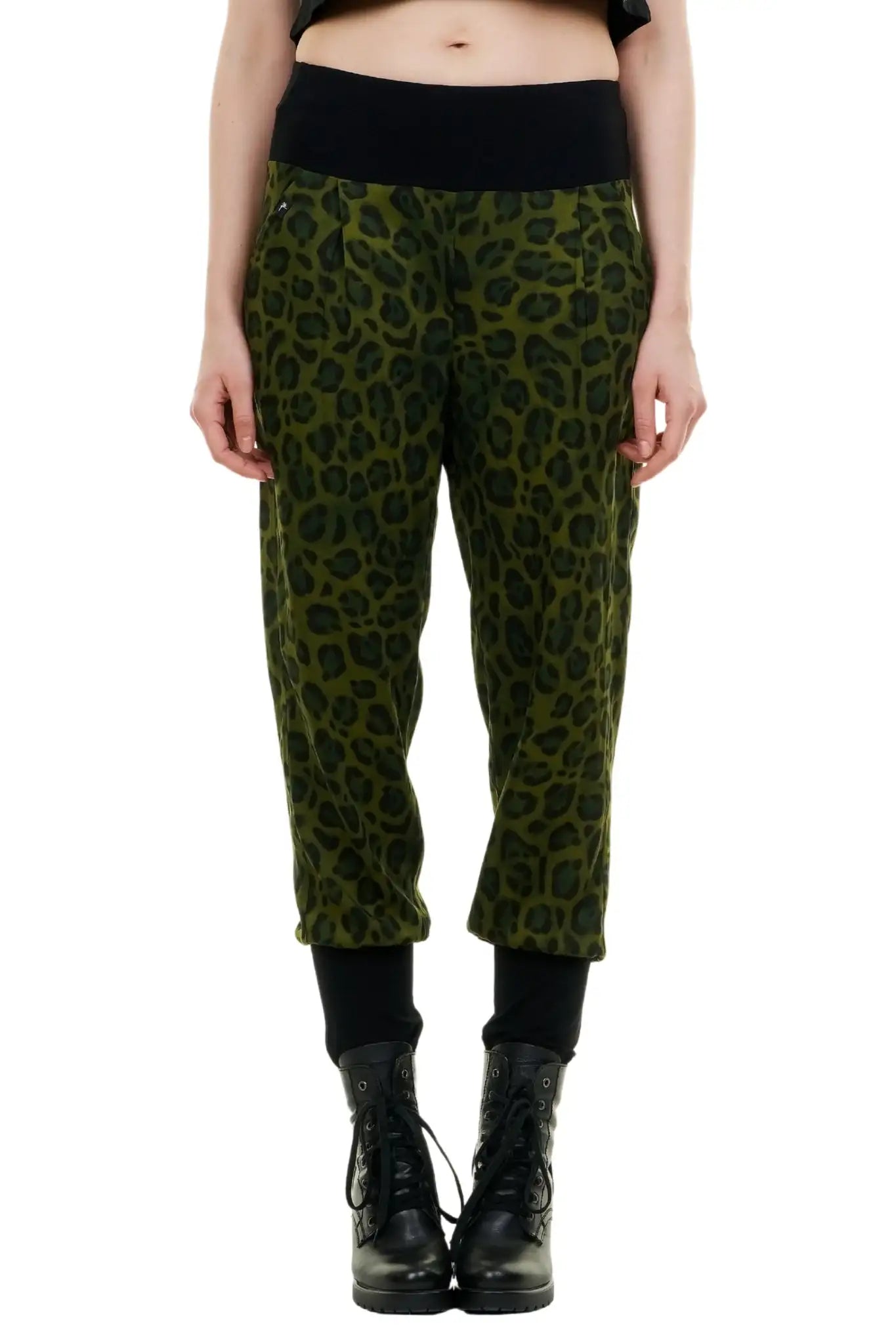 Frau präsentiert die grüne Baggy Fliederhose mit schwarzem Leopardenmuster, kombiniert mit einem schwarzen Crop-Top und schwarzen Schnürstiefeln. Die Hose aus leichtem Blusenstoff ist nachhaltig in Berlin hergestellt und hat einen tiefen Schritt sowie enge Knöchelbündchen