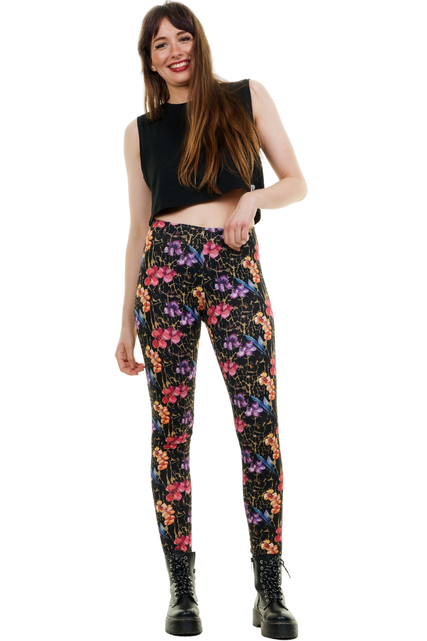 Ganzkörperansicht eines Models in blickdichten, schwarzen Baumwoll-Leggings mit buntem Blumenmuster. Kombiniert mit einem schwarzen ärmellosen Crop-Top und klobigen Schnürboots vor weißem Hintergrund. Model fasst sich lächelnd in die Haare und blickt zur Seite