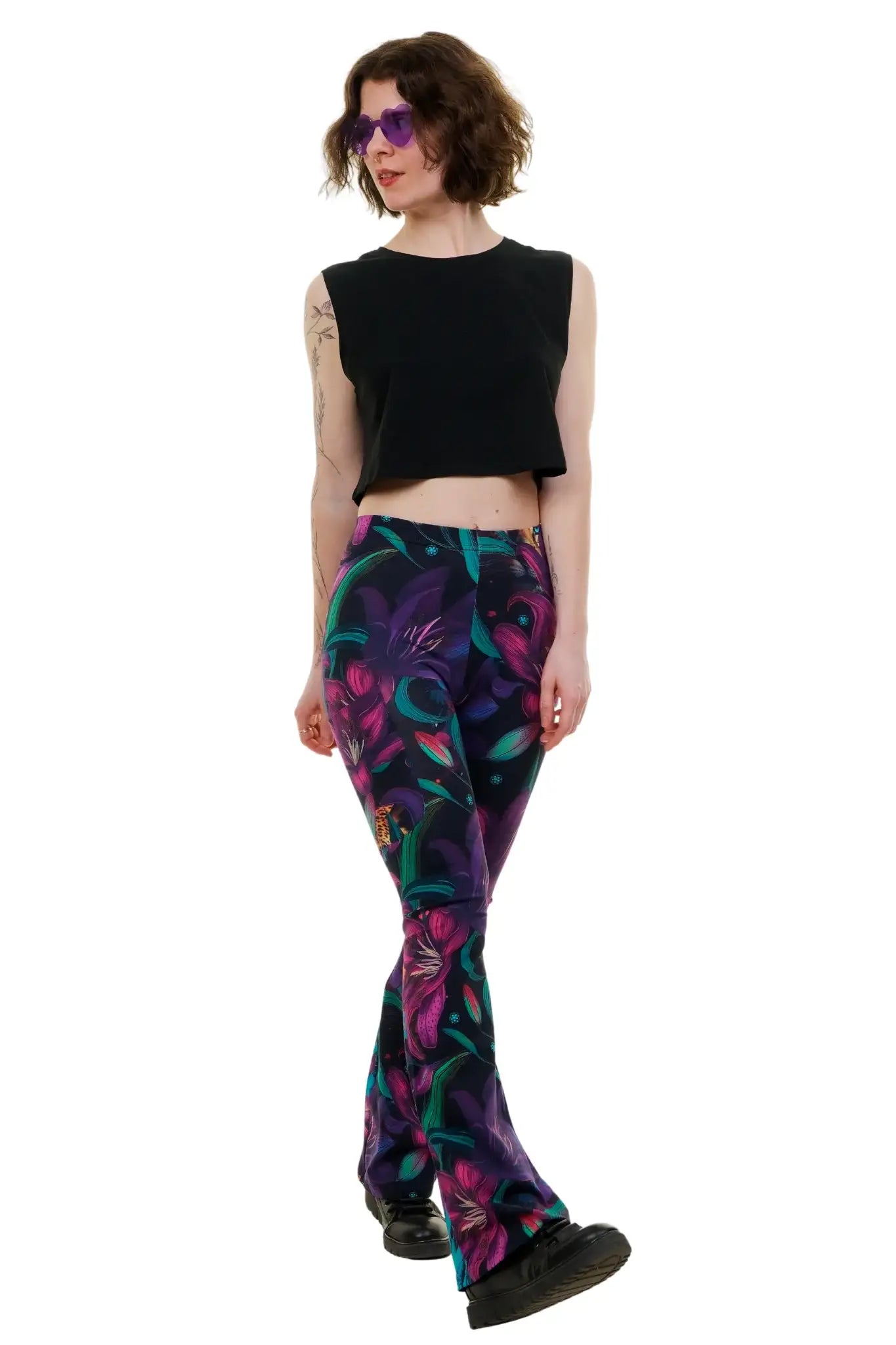 Frau mit schwarzem Crop Top, bunter Blumen-Leggings und lila Sonnenbrille auf weißem Hintergrund