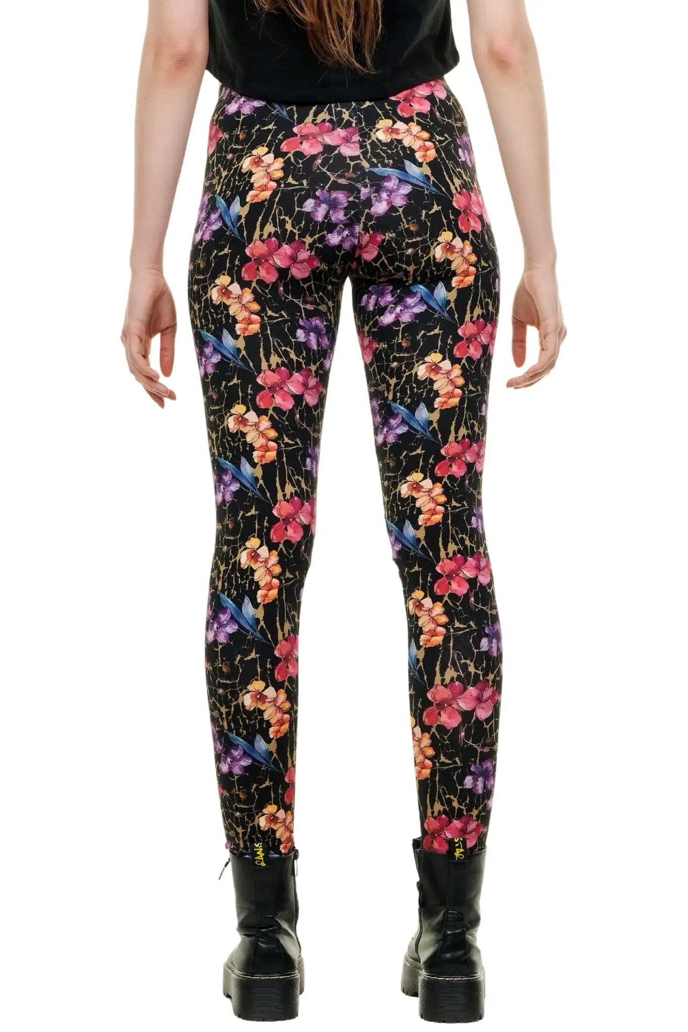 Das Model trägt die in Berlin handgefertigte Baumwoll-Leggings mit floralem Print. Das bunte Muster auf schwarzem Grund ist deutlich sichtbar. Sie steht in Schnürstiefeln und einem schwarzen Bauchfrei-Top, lächelnd und posebereit.
