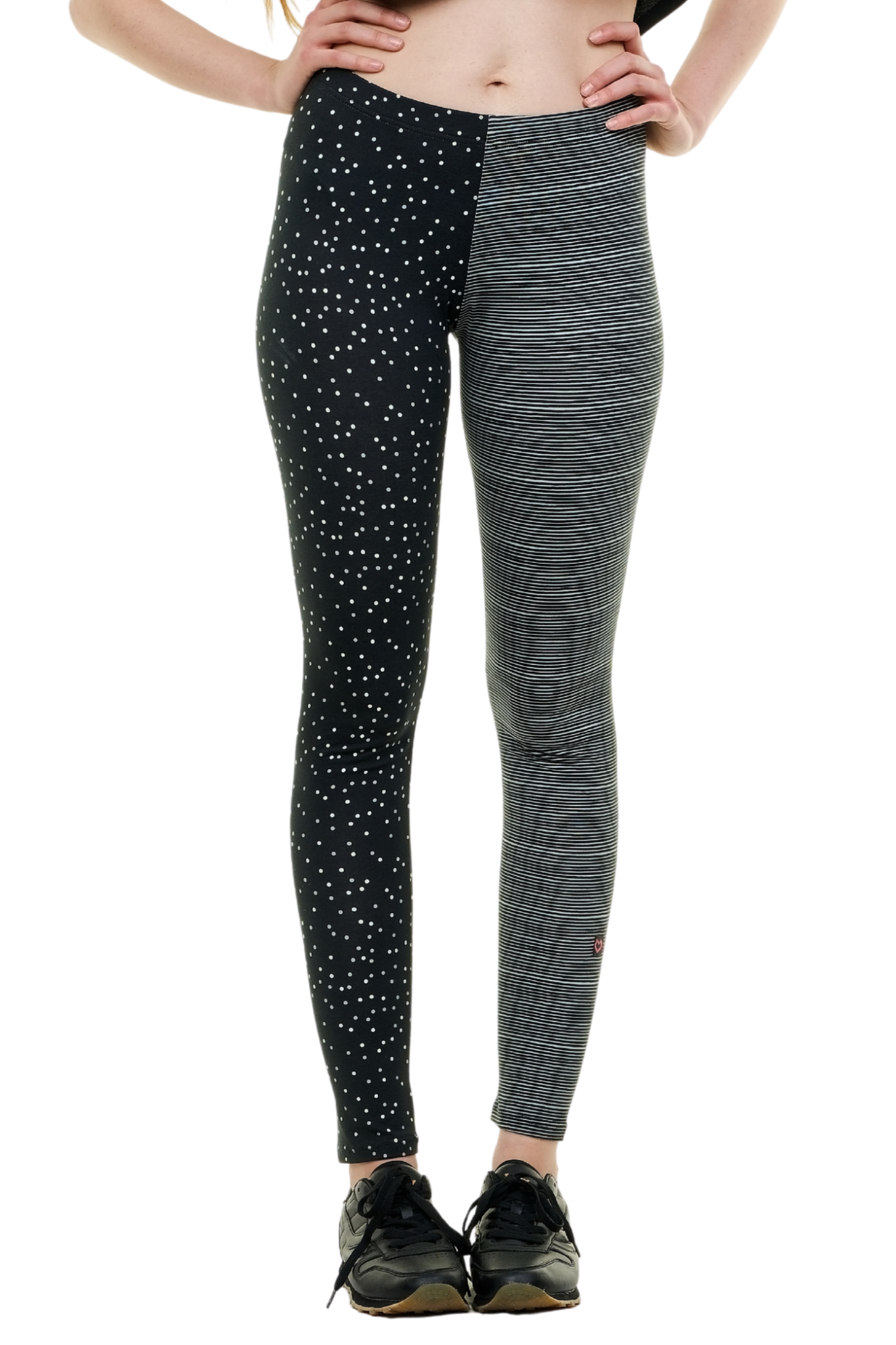 Detailansicht der Curlix Leggings mit schwarz-weißen horizontalen Streifen auf dem rechten Bein und einem weißen Punkte-Print auf dem linken Bein