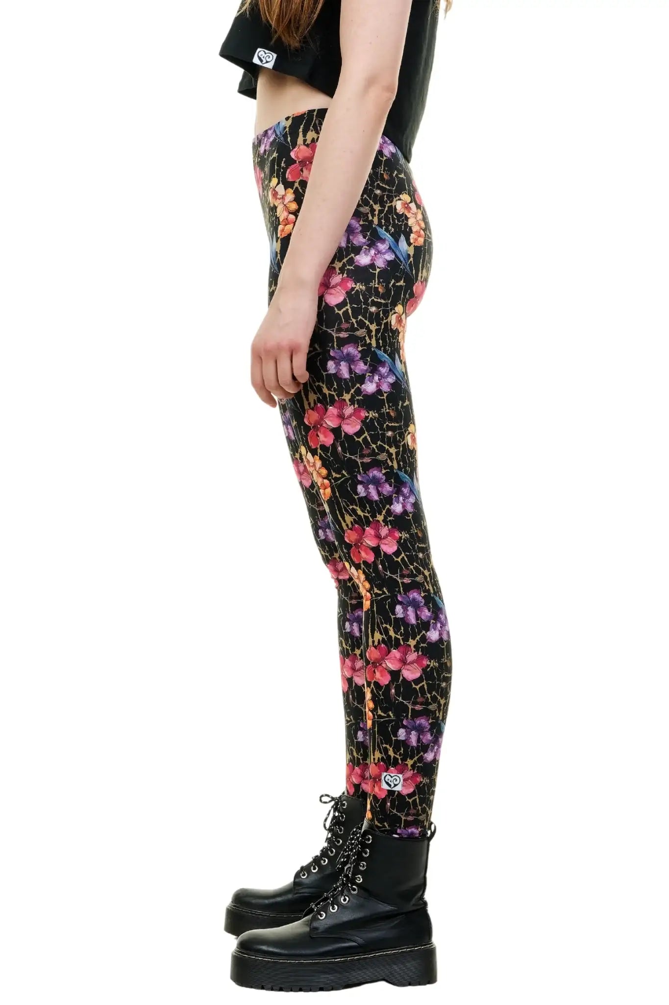 Nahaufnahme der Passform einer Baumwoll-Leggings mit intensivem Blumenmuster in Pink, Orange, Violett und Gelb auf schwarzem Stoff. Das Model steht mit leicht angewinkeltem Bein und zeigt den Stretch-Effekt und die Blickdichtigkeit der handgefertigten Hose