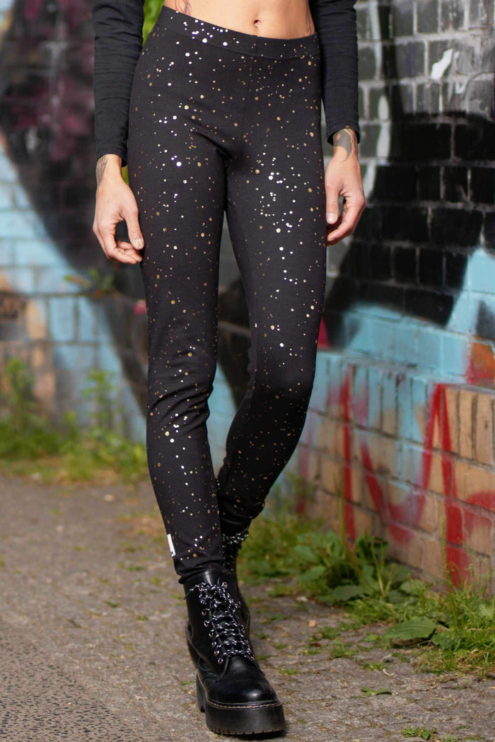 Schwarze Leggings mit goldenen Punkten, getragen draußen vor Graffiti-Wand, nachhaltige Mode