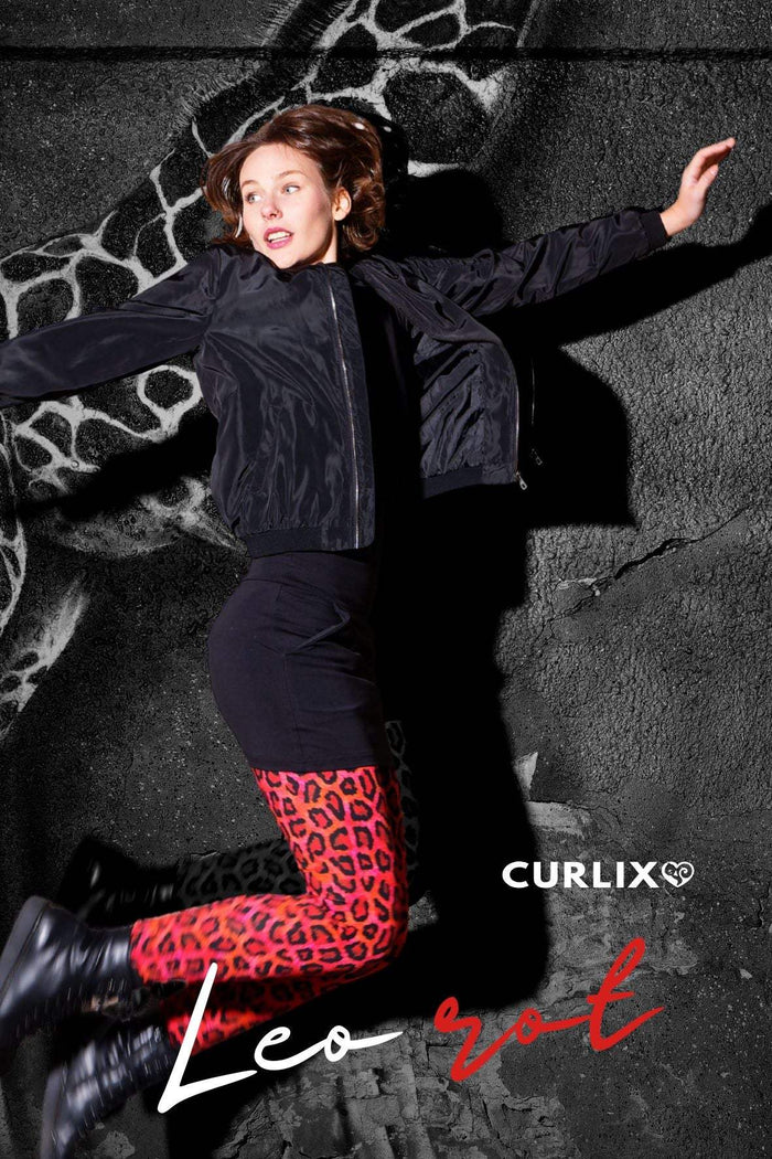 Frau mit roten Leggings im Leo-Print, schwarzer Jacke und Stiefeln vor gemustertem Hintergrund
