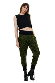 Frau trägt nachhaltige grüne Haremshose mit Leo-Print und schwarzem Crop-Top vor weißem Hintergrund.