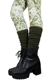 Olivgrüne Strickstulpen über gemusterten Leggings mit Blumen und Vögeln, kombiniert mit schwarzen Stiefeletten.