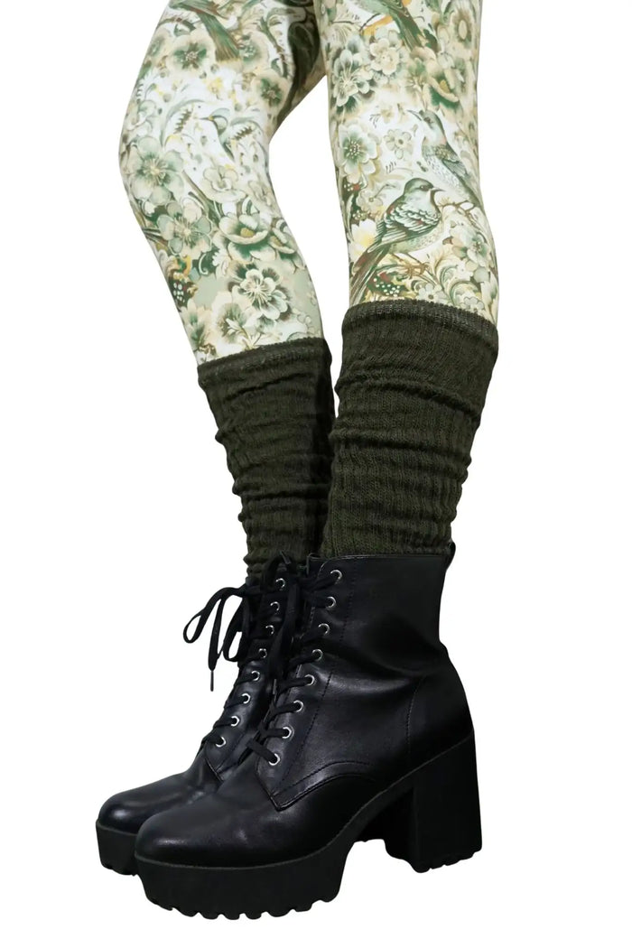 Olivgrüne Strickstulpen über gemusterten Leggings mit Blumen und Vögeln, kombiniert mit schwarzen Stiefeletten.